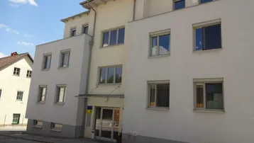 Modernes Mehrfamilienhaus mit heller Fassade und Rollläden an den Fenstern.