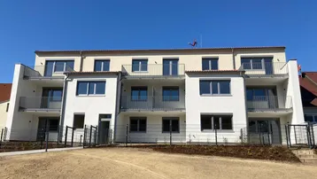 Moderne Fassade eines Neubaus mit mehreren Balkonen und klarem Himmel.
