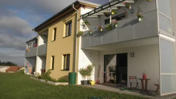 Gepflegter Gartenbereich mit Rasenfläche und Terrasse, ergänzt durch Balkone mit Blumenkästen.