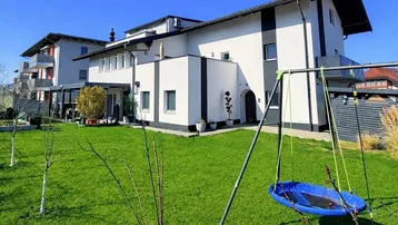 Großer Garten mit Rasenfläche und Kinderschaukel, ideal für Familien.