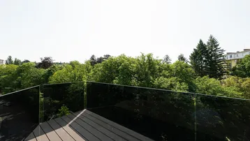 Sonnige Terrasse mit Glasgeländer und weitem Blick auf grüne Bäume und die Umgebung.