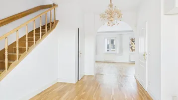 Heller Flur mit Holztreppe und elegantem Kronleuchter, der zu weiteren Räumen führt.
