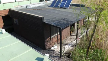 Hausboot von oben mit Solarmodulen auf dem Flachdach und umliegender Natur am Wasser.