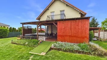 Ansicht des Hauses von hinten mit großem Garten, überdachter Terrasse und Balkon im Obergeschoss.