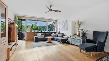 Helles Wohnzimmer mit Holzboden, großem Sofa und Blick in den grünen Garten.