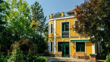 Elegante Villa mit leuchtend gelber Fassade, grünem Dach und privatem Pool im üppigen Garten.