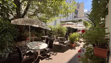 Gemütliche Außenterrasse mit Tischen, Stühlen und Sonnenschirmen unter grünen Bäumen.