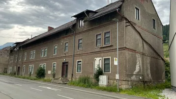 Ansicht der langen Fassade eines Mehrfamilienhauses mit mehreren Fenstern und einem Satteldach.