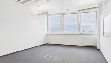 Leerer Büroraum mit Teppichboden, großen Fenstern und weitem Blick auf die Stadt.