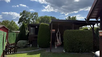 Gepflegter Gartenbereich mit Rasenfläche, Hecken und einer überdachten Terrasse mit Hängesessel.