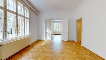 Helles Zimmer mit Fischgrätparkett und hohen Fenstern, das viel Tageslicht hereinlässt.