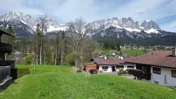 Weitläufige grüne Landschaft mit traditionellen Häusern und majestätischem Bergblick im Hintergrund.