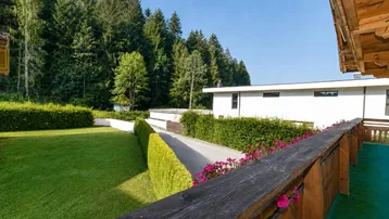 Blick vom Balkon auf den gepflegten Rasenbereich und die umgebende Natur mit Wald.