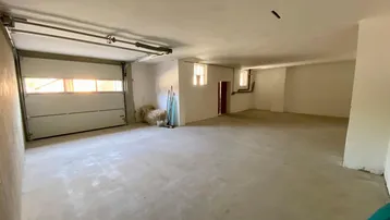 Geräumige Garage mit einem großen Garagentor, Betonboden und kleinen Fenstern, die Tageslicht hereinlassen.