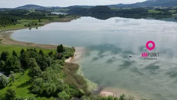 Luftaufnahme eines malerischen Sees umgeben von grüner Landschaft und sanften Hügeln, ideal für Naturliebhaber.