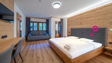 Geräumiges Schlafzimmer mit Holzboden, Doppelbett, Sofa und Schreibtischbereich, hell und modern eingerichtet.
