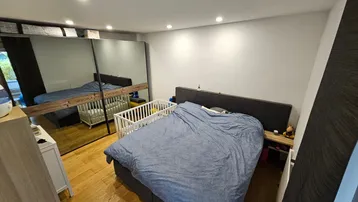 Helles Schlafzimmer mit Holzboden, großem Spiegelschrank und Babybett, das eine gemütliche Atmosphäre schafft.