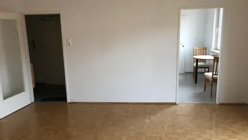 Helles Wohnzimmer mit Parkettboden und zwei Türöffnungen zu weiteren Räumen.