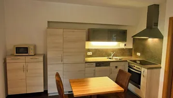 Funktionale Küche mit Holzschränken, integrierten Geräten und einem kleinen Essbereich für zwei Personen.
