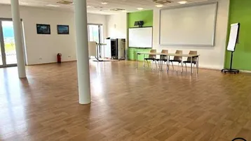 Großer, heller Konferenzraum mit Holzboden, Projektionsflächen und Blick ins Grüne.