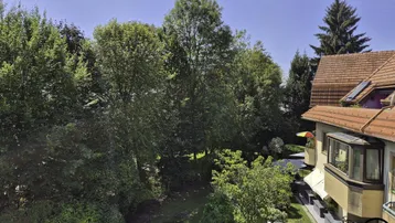 Blick auf die Rückseite des Gebäudes mit üppiger Baumlandschaft und Terrassenbereichen.