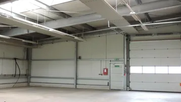 Geräumige Lagerhalle mit hohen Decken, Betonboden und einem großen Rolltor für den Zugang.