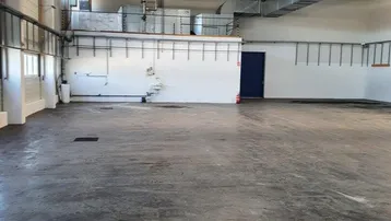 Geräumige Lagerhalle mit hohen Decken, Betonboden und sichtbaren Lüftungsrohren, ideal für industrielle Nutzung.