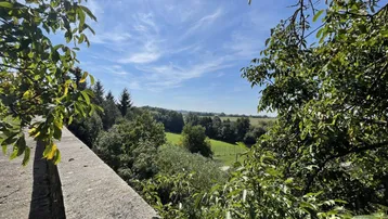 Weitläufiger Blick über die grüne Landschaft und Felder unter strahlend blauem Himmel.