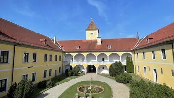 Historischer Innenhof eines Schlosses mit zentralem Brunnen und gepflegter Grünfläche unter blauem Himmel.