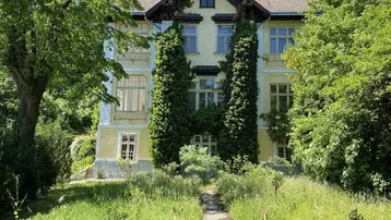 Prächtige historische Villa mit gepflegtem Vorgarten und üppiger Vegetation an einem sonnigen Tag.