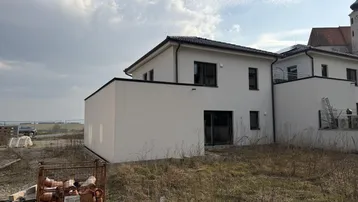 Rückseite eines Neubauhauses mit Blick auf eine Kirche und die umliegende Landschaft.