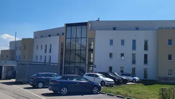 Modernes Mehrfamilienhaus mit Glasfassade und Außenparkplätzen unter blauem Himmel.