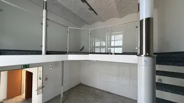 Geräumiger Innenraum mit Galerie, Glasgeländer und Betonboden, ideal für gewerbliche Nutzung.