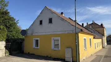Altes Haus mit gelber Fassade und weißem Giebel unter blauem Himmel.