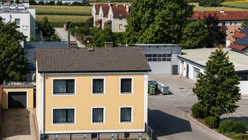 Ansicht eines gelben Einfamilienhauses von der Straße mit ländlicher Umgebung im Hintergrund.