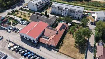Luftaufnahme eines Anwesens mit mehreren Gebäuden, Parkplätzen und Solaranlagen auf den Dächern.