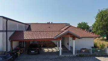 Einfamilienhaus mit überdachtem Carport, Ziegeldach und Holzstapel im Freien unter blauem Himmel.