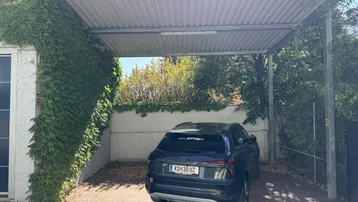 Überdachter Stellplatz (Carport) mit Efeu bewachsener Wand und geparktem Fahrzeug.