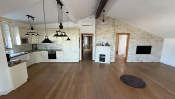 Offener Wohnbereich mit integrierter Küche, Holzboden und Dachschrägen, inklusive Kamin und TV-Wand.