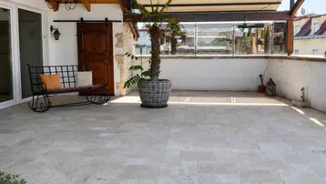 Geräumige Terrasse mit Fliesenboden, Sitzbank und einer Palme, ideal zum Entspannen im Freien.