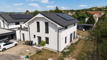 Modernes Einfamilienhaus mit Photovoltaikanlage und gepflegtem Vorgarten unter blauem Himmel.
