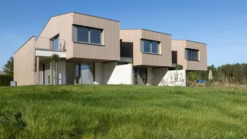 Moderne Reihenhäuser mit Holzfassade und großzügiger Grünfläche in ländlicher Umgebung.