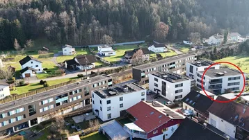 Luftaufnahme einer Wohnsiedlung mit mehreren Gebäuden und umliegender Naturlandschaft.