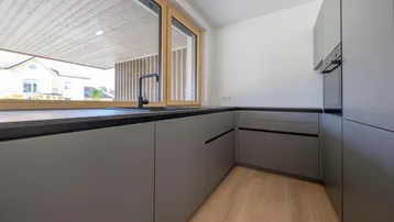 Moderne Küche mit grauen Schränken, dunkler Arbeitsplatte und großem Fenster.