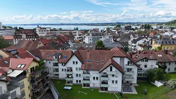 Panoramablick über die Stadt mit Wohngebäuden, grünen Flächen und einem See im Hintergrund.