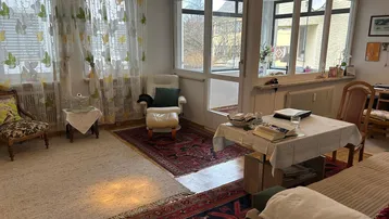 Gemütliches Wohnzimmer mit Teppichen, bequemen Möbeln und Zugang zu einem verglasten Balkon.