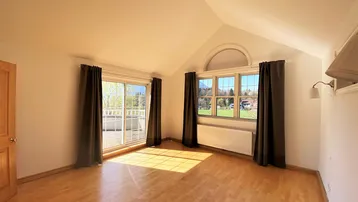 Helles Zimmer mit Holzboden, hohen Decken und Zugang zu einem Balkon mit Bergblick.