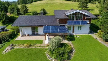 Haus mit Solaranlage, gepflegtem Garten und weitem Blick auf die grüne Hügellandschaft.