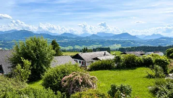 Weitläufiger Panoramablick über eine ländliche Siedlung mit Bergen im Hintergrund unter blauem Himmel.