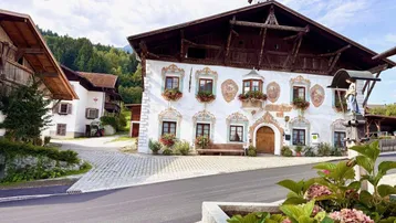 Traditionelles Gebäude mit bemalter Fassade und Holzbalkonen in einer ländlichen Umgebung mit Bergblick.